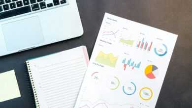 Flatlay of business report with colorful charts, a notebook, and a laptop for data analysis on a desk.