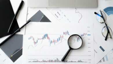 Flat lay of stock market analysis documents with magnifying glass, pens, and glasses.