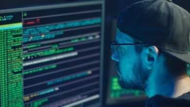 A cybersecurity expert inspecting lines of code on multiple monitors in a dimly lit office.