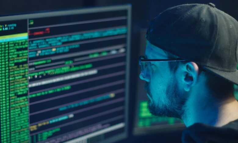 A cybersecurity expert inspecting lines of code on multiple monitors in a dimly lit office.