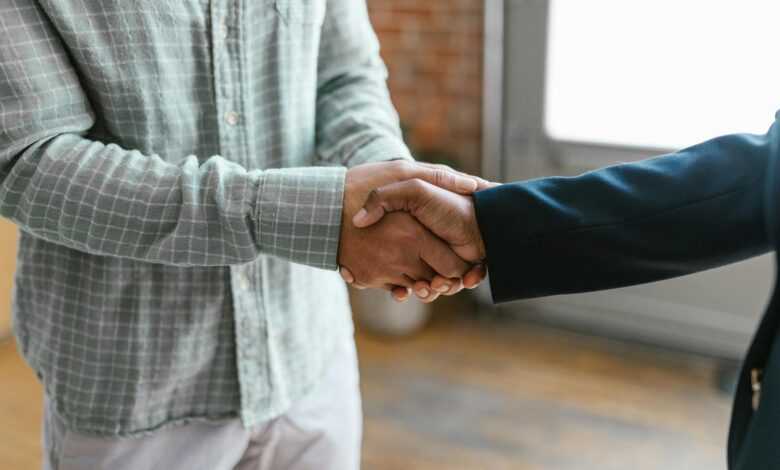 Close-up of two business professionals shaking hands in a modern office environment.