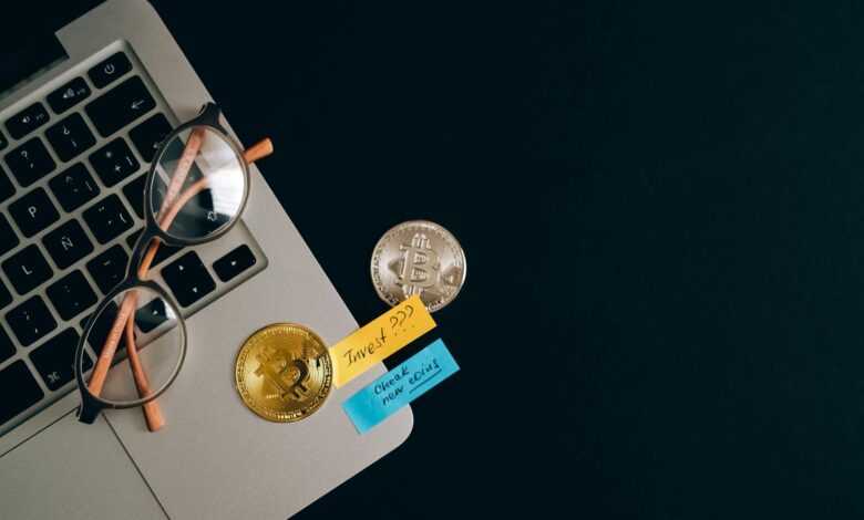 Laptop, bitcoins, and notes on a desk representing cryptocurrency investment concept.