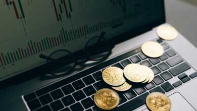 Golden Bitcoins on a laptop keyboard with a stock market chart on the screen, symbolizing cryptocurrency trading.