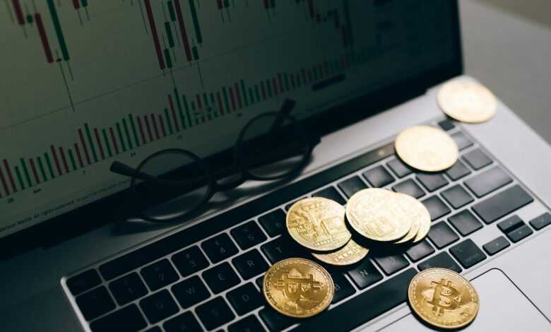 Golden Bitcoins on a laptop keyboard with a stock market chart on the screen, symbolizing cryptocurrency trading.