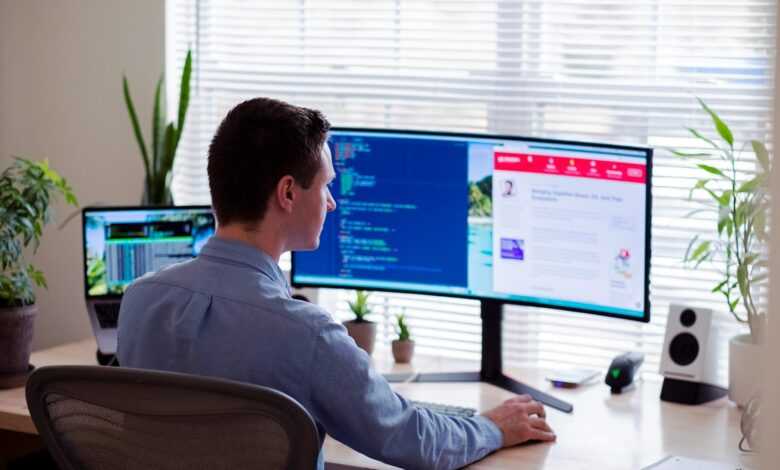 man in gray dress shirt sitting on chair in front of computer monitor